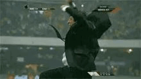 a man in a suit and tie is jumping in the air while watching a soccer game .