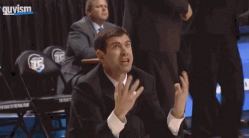A Man In A Suit And Tie Is Kneeling On The Floor During A Basketball Game GIF