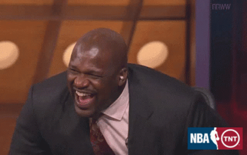 A Man In A Suit And Tie Is Laughing In Front Of An Nba Logo GIF