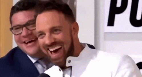 A Man In A Suit And Tie Is Laughing Next To Another Man In A White Jacket . GIF