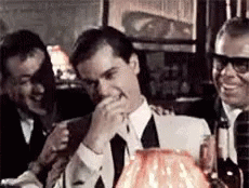 A Man In A Suit And Tie Is Laughing While Sitting At A Table In A Restaurant . GIF