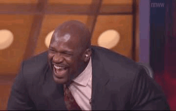 A Man In A Suit And Tie Is Laughing While Sitting In A Chair . GIF