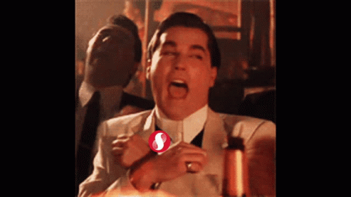 A Man In A Suit And Tie Is Laughing With A Red S On His Shirt GIF