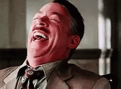 A Man In A Suit And Tie Is Laughing With His Eyes Closed And His Mouth Open . GIF