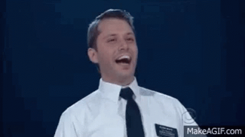 A Man In A Suit And Tie Is Laughing With His Mouth Open . GIF