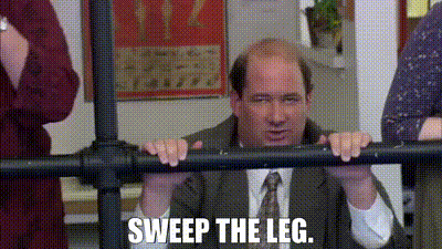 A Man In A Suit And Tie Is Leaning Against A Railing And Saying `` Sweep The Leg . '' GIF
