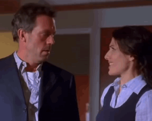 A Man In A Suit And Tie Is Looking At A Woman In A Blue Shirt . GIF