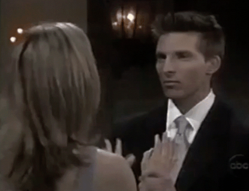 A Man In A Suit And Tie Is Looking At A Woman In A Dress GIF