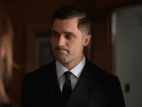 A Man In A Suit And Tie Is Looking At A Woman . GIF