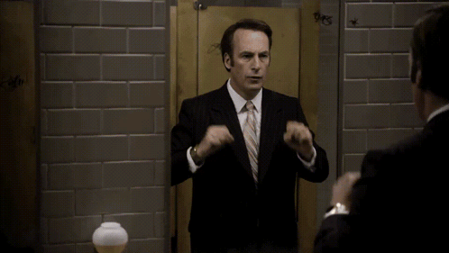 A Man In A Suit And Tie Is Looking At Himself In A Bathroom Stall With The Word Days Written On The Wall GIF