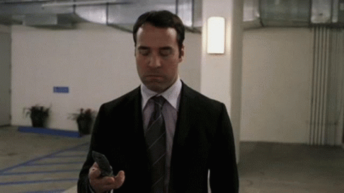 A Man In A Suit And Tie Is Looking At His Cell Phone . GIF