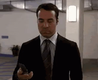 A Man In A Suit And Tie Is Looking At His Cell Phone . GIF