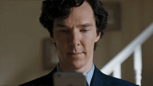 A Man In A Suit And Tie Is Looking At His Phone GIF