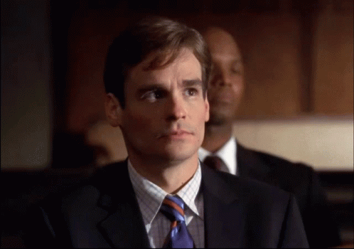 A Man In A Suit And Tie Is Looking At Something GIF