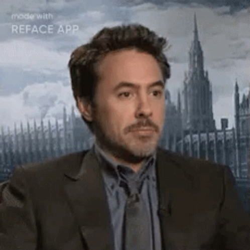A Man In A Suit And Tie Is Looking At The Camera With A Castle In The Background . GIF