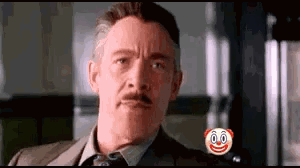 A Man In A Suit And Tie Is Looking At The Camera With A Clown Face On His Chest . GIF