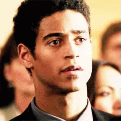 A Man In A Suit And Tie Is Looking At The Camera With A Group Of People In The Background . GIF