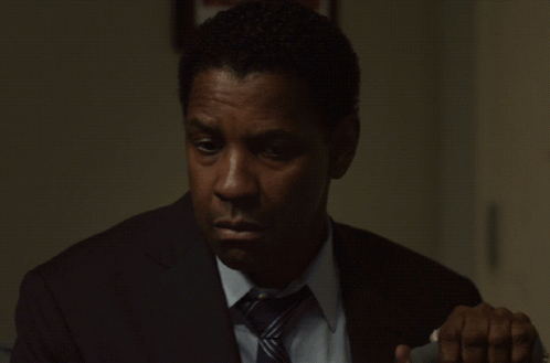 A Man In A Suit And Tie Is Looking Down At Something GIF