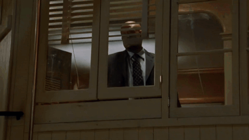 A Man In A Suit And Tie Is Looking Out A Window GIF