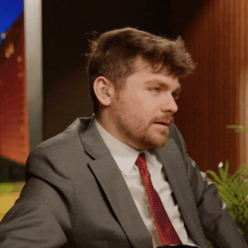 A Man In A Suit And Tie Is Looking To His Left GIF
