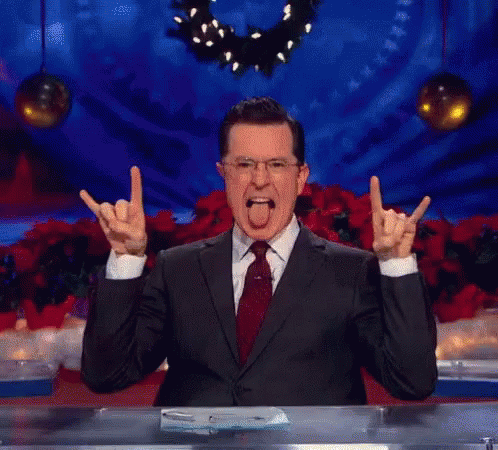 A Man In A Suit And Tie Is Making A Devil Horns Sign With His Hands GIF