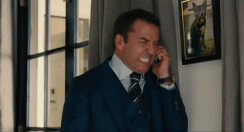 A Man In A Suit And Tie Is Making A Face While Talking On A Cell Phone GIF