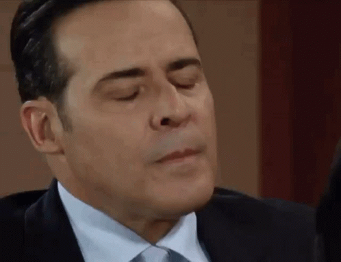 A Man In A Suit And Tie Is Making A Face With His Eyes Closed . GIF