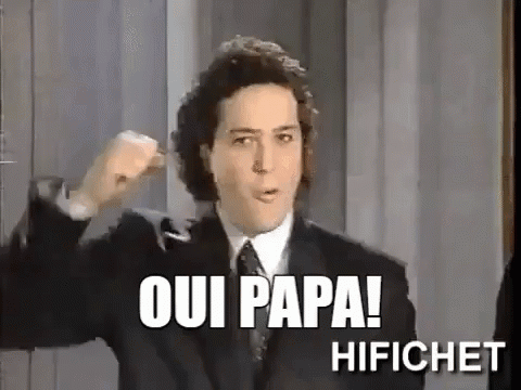 A Man In A Suit And Tie Is Making A Fist In The Air And Says Oui Papa ! GIF