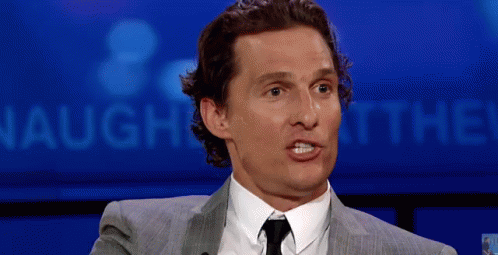A Man In A Suit And Tie Is Making A Funny Face In Front Of A Sign That Says Laugh At The ! GIF