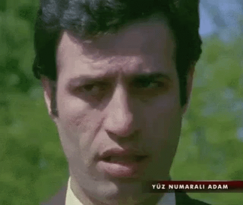 A Man In A Suit And Tie Is Making A Funny Face In Front Of Trees . GIF