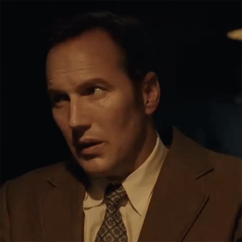 A Man In A Suit And Tie Is Making A Funny Face In The Dark . GIF