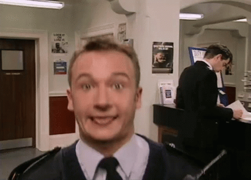 A Man In A Suit And Tie Is Making A Funny Face While Another Man Stands Behind Him . GIF