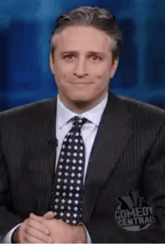 A Man In A Suit And Tie Is Making A Funny Face While Giving A Thumbs Up . GIF