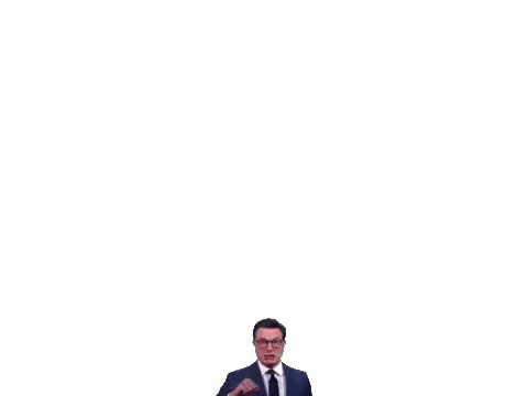 A Man In A Suit And Tie Is Making A Funny Face While Pointing At The Camera . GIF