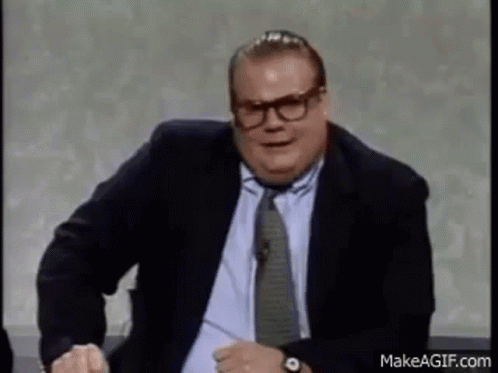A Man In A Suit And Tie Is Making A Funny Face While Sitting On A Chair . GIF