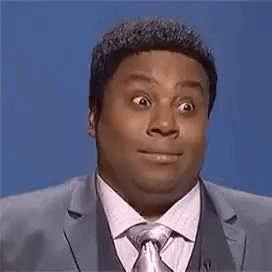 A Man In A Suit And Tie Is Making A Funny Face While Standing In Front Of A Blue Background . GIF