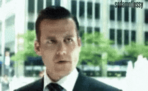 A Man In A Suit And Tie Is Making A Funny Face While Standing In Front Of A Building . GIF