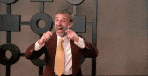 A Man In A Suit And Tie Is Making A Funny Face While Standing In Front Of A Wall . GIF