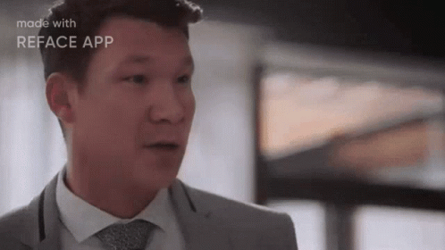 A Man In A Suit And Tie Is Making A Funny Face While Standing In Front Of A Window . GIF