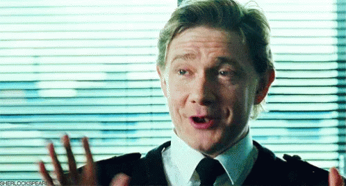 A Man In A Suit And Tie Is Making A Funny Face While Standing In Front Of A Window With Blinds . GIF