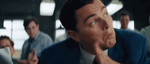 A Man In A Suit And Tie Is Making A Funny Face With His Finger On His Chin GIF