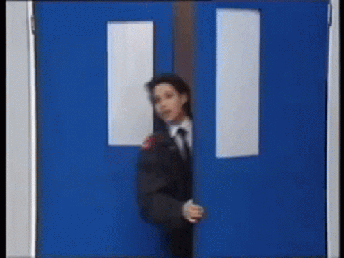 A Man In A Suit And Tie Is Peeking Out From Behind A Blue Door GIF