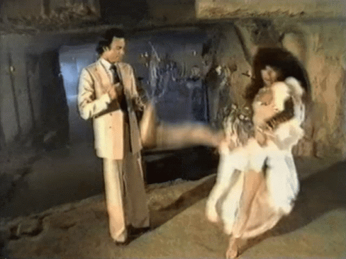 A Man In A Suit And Tie Is Pointing At A Woman In A White Dress GIF