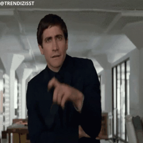 A Man In A Suit And Tie Is Pointing At Something With The Hashtag Trendizisst GIF