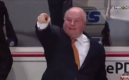 A Man In A Suit And Tie Is Pointing At The Camera In Front Of A Sign That Says Nbc On It GIF