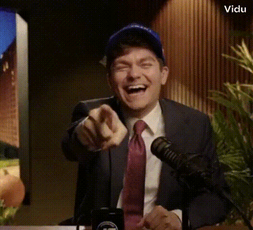 A Man In A Suit And Tie Is Pointing At The Camera While Laughing GIF