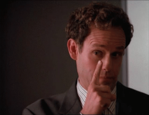 A Man In A Suit And Tie Is Pointing His Finger At His Nose GIF