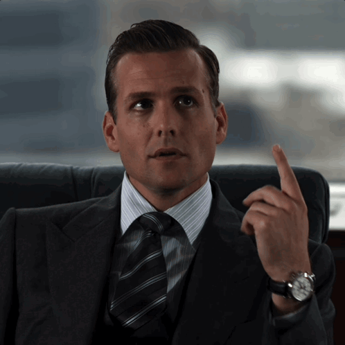 A Man In A Suit And Tie Is Pointing His Finger Up GIF