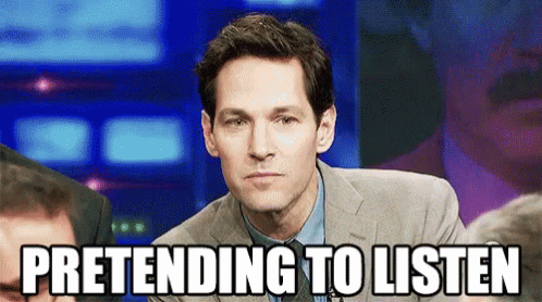 A Man In A Suit And Tie Is Pretending To Listen While Sitting In Front Of A Crowd . GIF