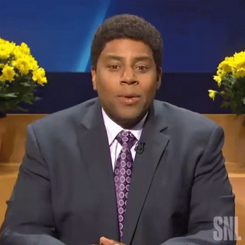 A Man In A Suit And Tie Is Saying Boo While Sitting On A Stage . GIF